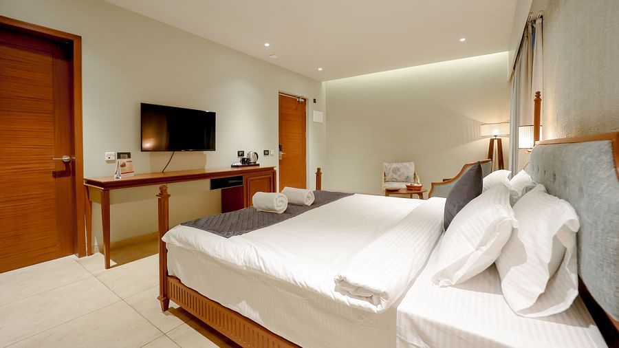 An image of a bedroom featuring a bed, flat TV screen, table below it and other furniture - Pride Resort Ambaji